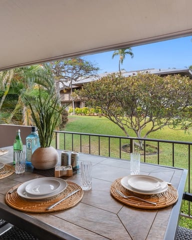 Covered patio with dining table set for two, overlooking tropical garden and golf course with palm trees