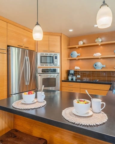 Modern kitchen with wood cabinetry, stainless steel appliances, black countertop, and open shelving displaying decorative fish figurines.
