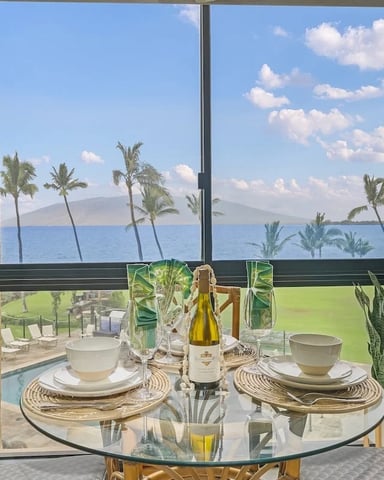 Dining room with round glass table, wooden chairs, ocean and palm tree views through floor-to-ceiling windows