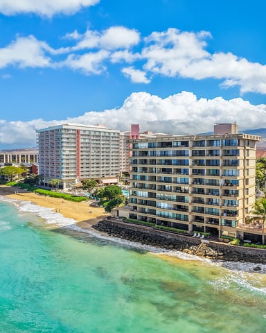 Beachfront resort buildings along sandy beach with turquoise ocean and West Maui mountains in background