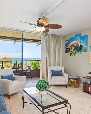Coastal living room with ocean view, blue and cream seating, ceiling fan, and beach-themed wall art