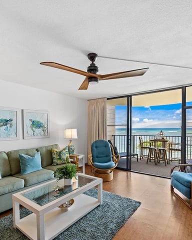 Beachfront living room with ocean view, green sofa, ceiling fan, and glass doors opening to balcony