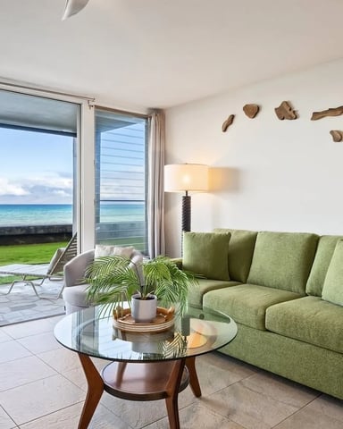 Beachfront living room with green sofa, glass doors opening to ocean view, and driftwood wall art