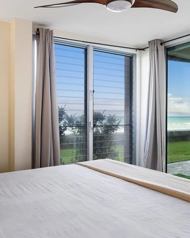 Bedroom with queen bed and glass doors opening to lawn, ocean, and beach view