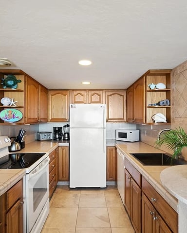 Galley kitchen with wood cabinets, white appliances, beige tile backsplash, and champagne bottle on counter