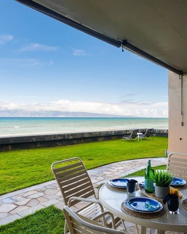 Beachfront patio with dining table, lounge chairs, ocean view, and palm trees under concrete overhang