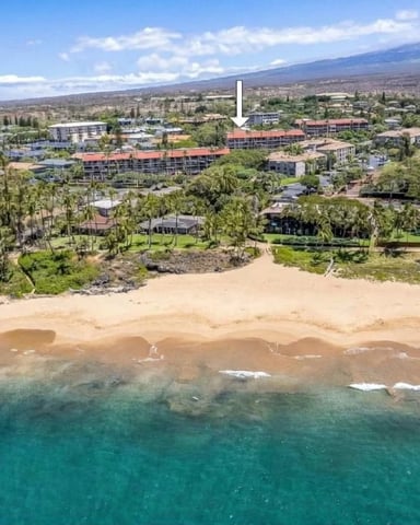 Aerial view of beachfront resort with sandy beach, turquoise water, palm trees, and buildings with red roofs along coastline