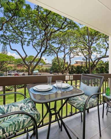 Lanai with dining table, lounge chairs, and view of large spreading trees, lawn, and distant ocean