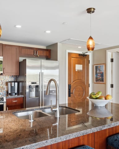 Modern kitchen with wood cabinets, granite countertops, stainless steel appliances, colorful tile backsplash, and pendant lighting over island