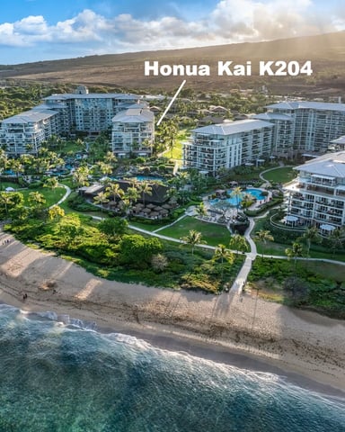 Aerial view of beachfront resort complex with multi-story white buildings, pools, and landscaped grounds along sandy beach and ocean