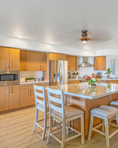 Modern kitchen with wood cabinets, stainless steel appliances, large island with seating, and white shuttered windows