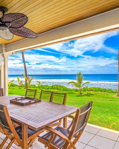 Covered patio with dining table overlooking ocean, beach, and palm trees