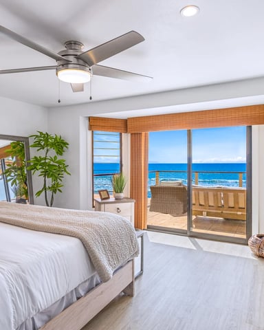 Bright bedroom with queen bed, ceiling fan, and glass doors opening to ocean-view balcony with wooden railings