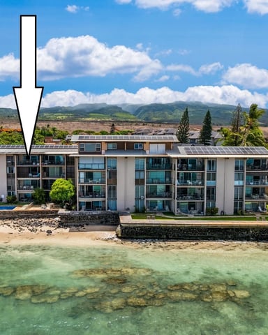 Beachfront condominium complex with white arrow pointing to left unit, turquoise ocean and mountains in background