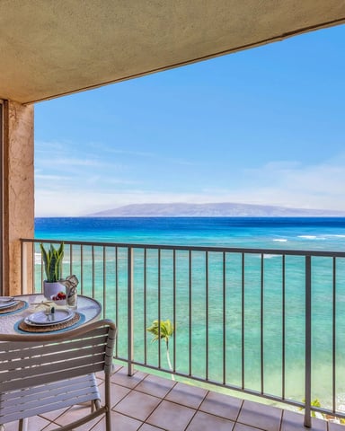 Oceanfront balcony with dining table, lounge chairs, and turquoise water view with distant island