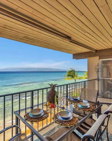 Beachfront lanai with dining table, lounge chairs, and ocean view overlooking turquoise water and sandy beach