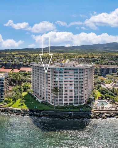 Beachfront condominium complex with arrow pointing to central building, ocean and green valley landscape beyond