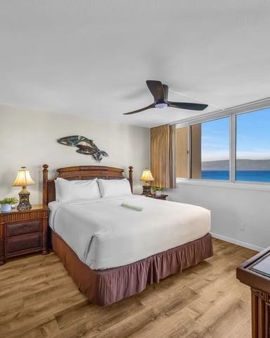 Bedroom with wooden four-poster bed, ocean view through large windows, ceiling fan, and coastal decor