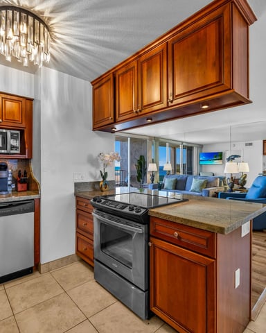 Open-plan kitchen and living room with wood cabinets, island, stainless steel appliances, and ocean view through large windows