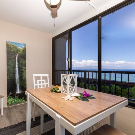 Dining room with ocean view through sliding glass doors, wooden table, white chairs, and waterfall artwork on wall