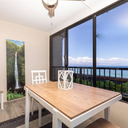 Dining room with ocean view through sliding glass doors, wooden table, white chairs, and waterfall artwork on wall