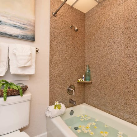 Bathroom with cork shower walls, white toilet with potted plant, towel rack, and bathtub filled with green water and yellow flowers