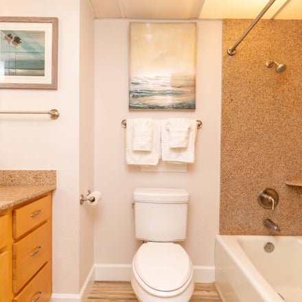 Bathroom with yellow vanity, cork countertop, white toilet, and cork-tiled shower enclosure with ocean artwork