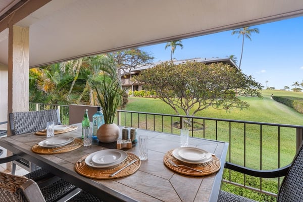 Covered patio with dining table set for two, overlooking manicured lawn and tropical trees