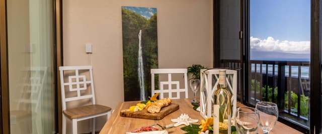 Dining table with food and wine overlooking ocean view from balcony with waterfall artwork on wall